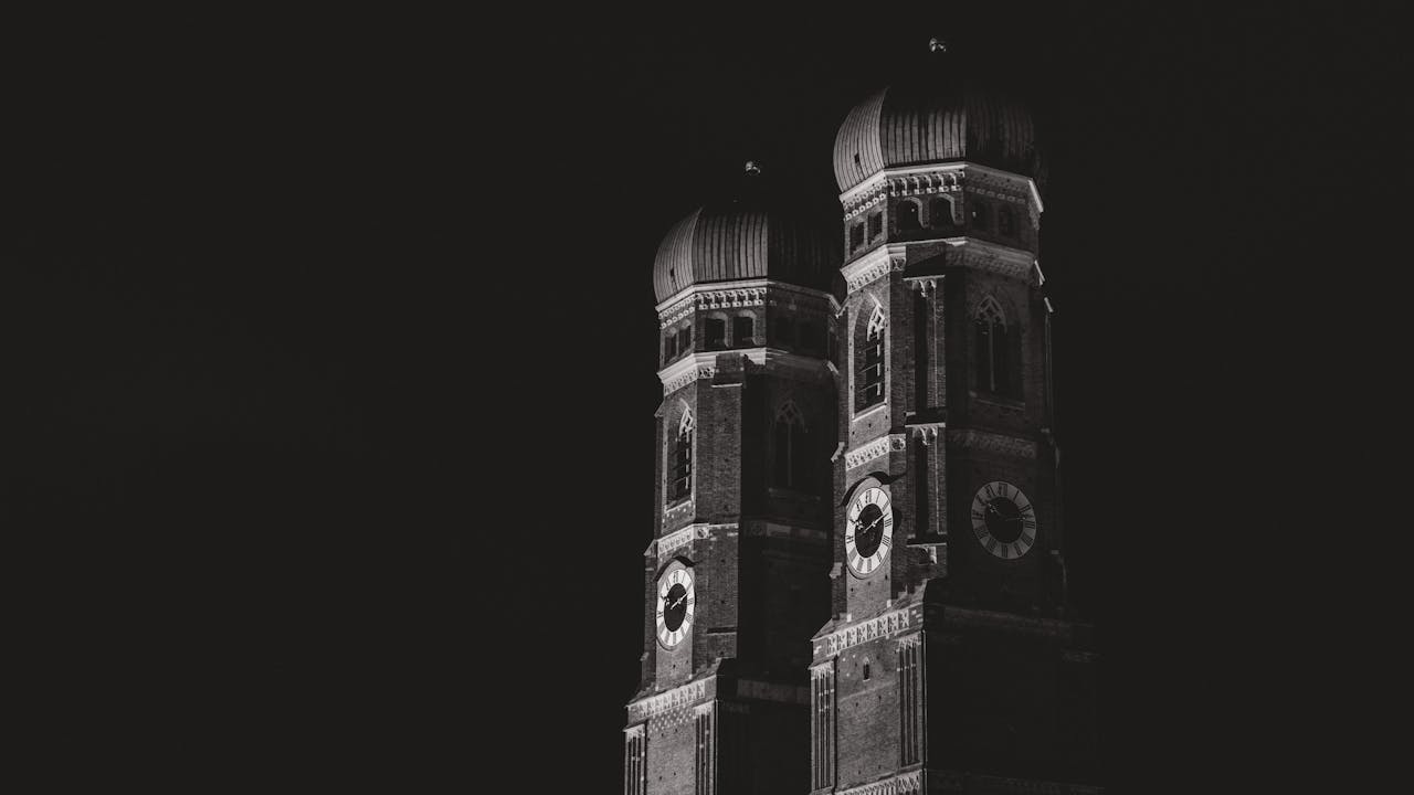 Black and white photograph of Frauenkirche towers illuminated at night in Munich, Germany.